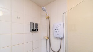 Una ducha con cabezal de ducha manual, panel de control en la pared y dispensador de jabón.
