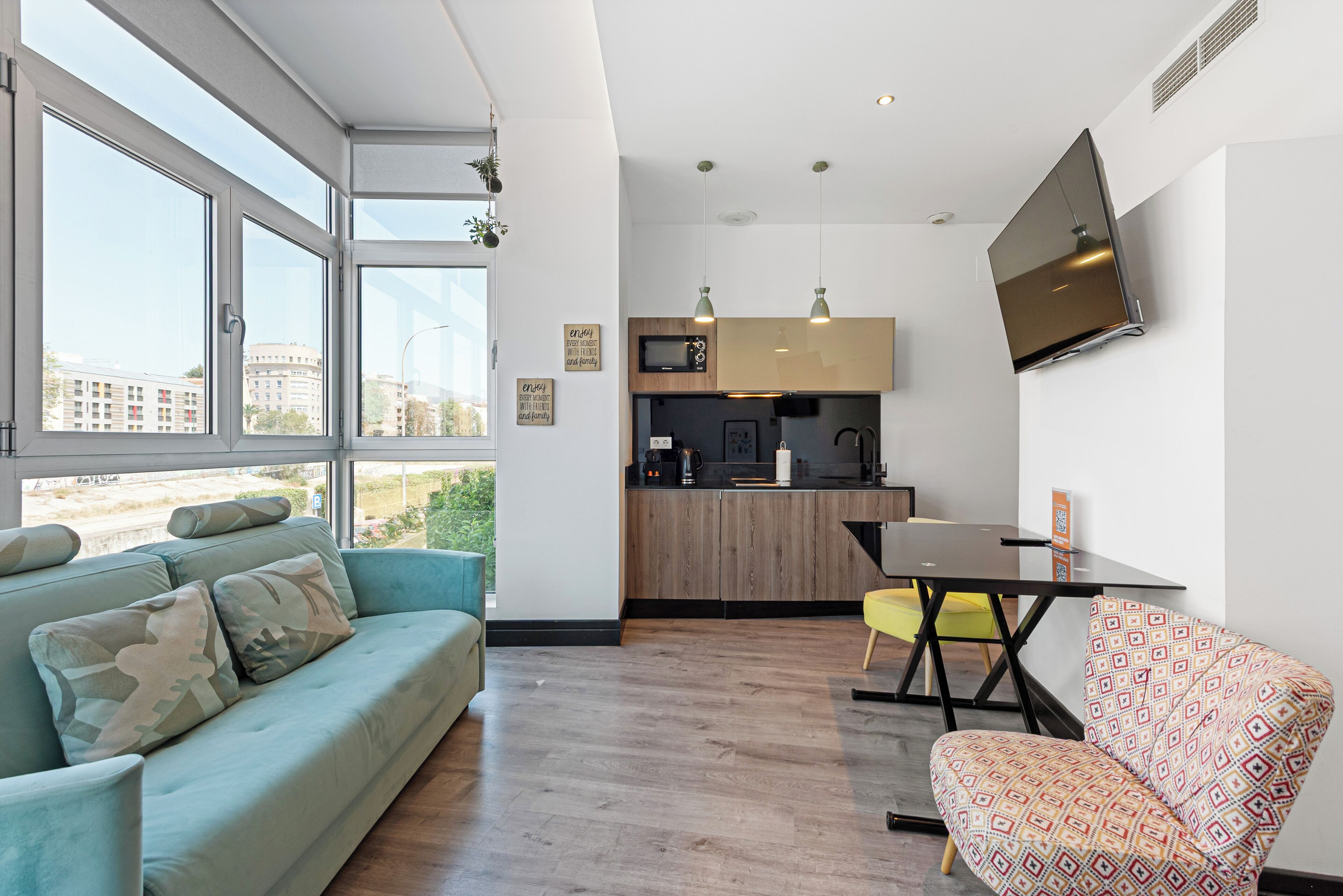 Un espacio habitable moderno con sofá, un sillón estampado, una mesa de comedor, una zona de cocina y un amplio ventanal con vista a la ciudad.