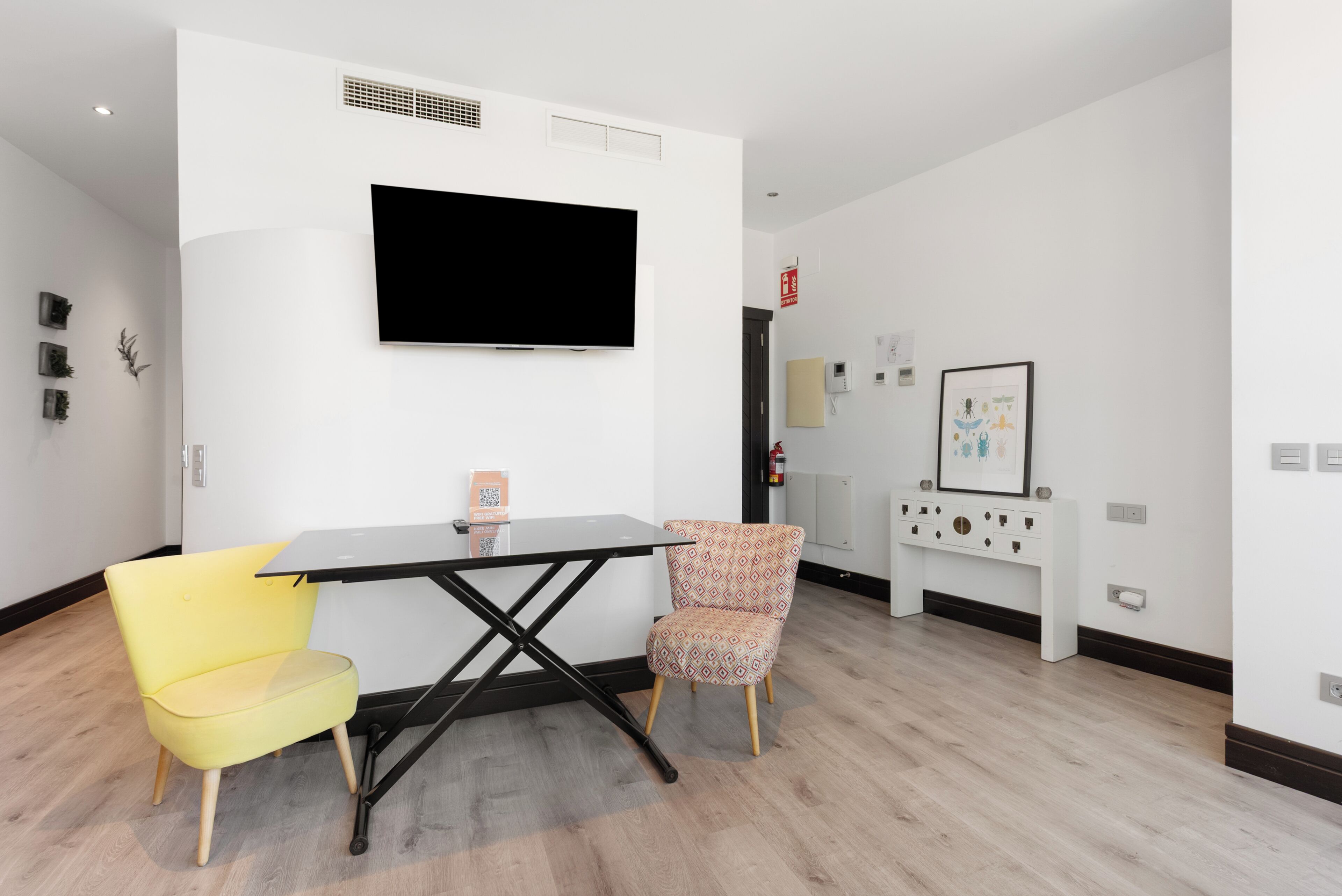 A modern room with a flat-screen TV, a small table, two chairs, a white console, and a framed picture on the wall.