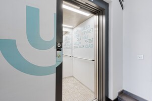 Un ascenseur orné d’un grand logo en forme de « U » et sur lequel sont affichés des panneaux de bienvenue multilingues.