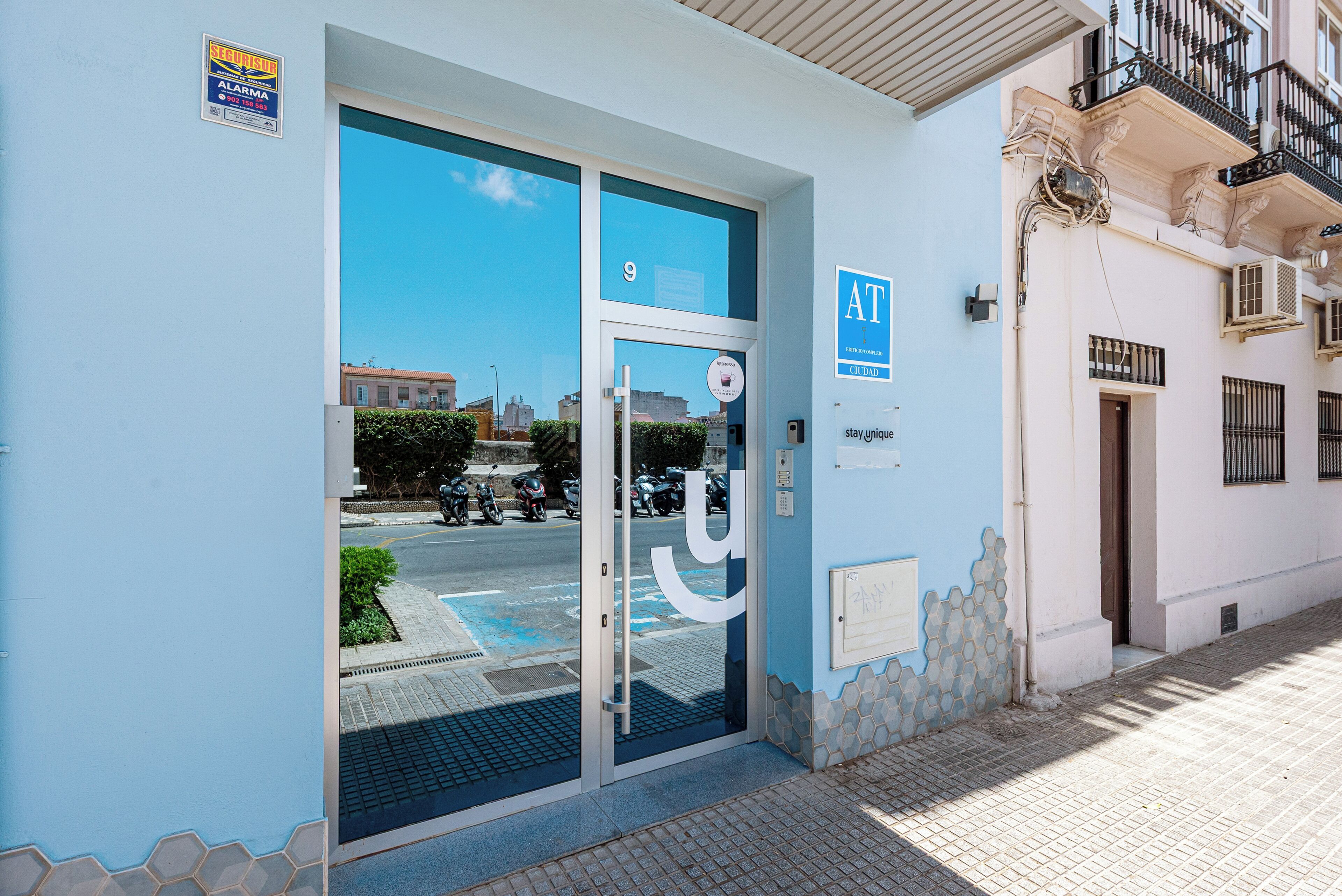 A building entrance with a glass door, a sign indicating the number 9, and a blue sign with 'AT' and 'CILIBAU' on the wall.