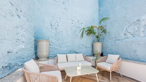 Ein Zimmer mit blauer Wandstruktur, einem Sofa, zwei Korbstühlen, einem Couchtisch und zwei großen Pflanzgefäßen.