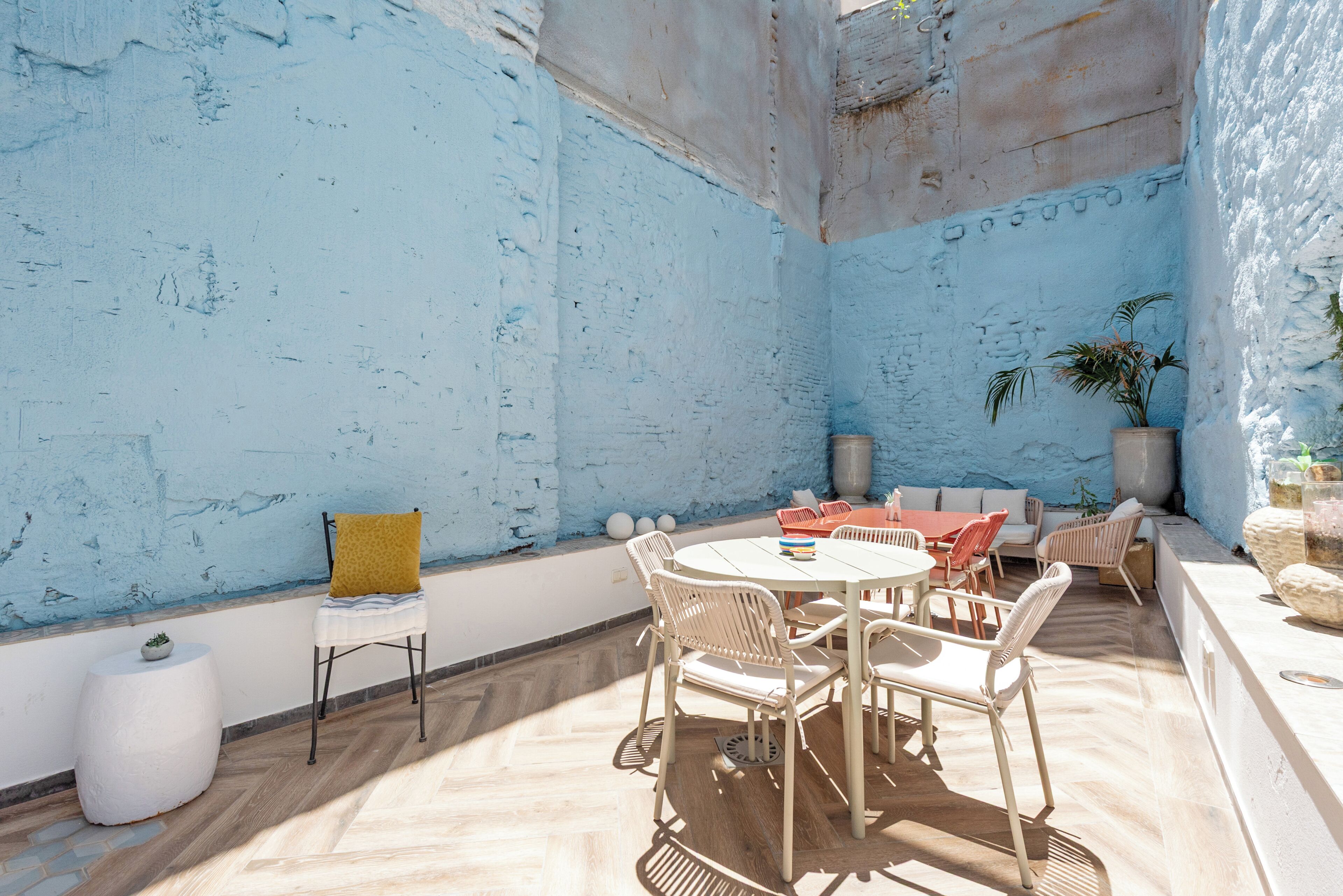 Un espace extérieur ensoleillé, aménagé avec une table ronde et des chaises, un canapé et un pot de fleurs.