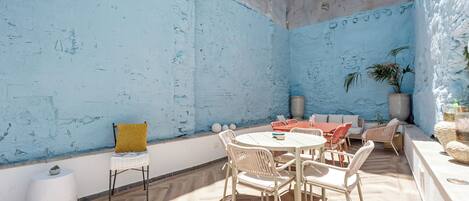 Un espace extérieur ensoleillé, aménagé avec une table ronde et des chaises, un canapé et un pot de fleurs.