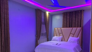 Egy hálószoba, amelyben ágy, függönyök és LED-es világítással ellátott mennyezet található.
