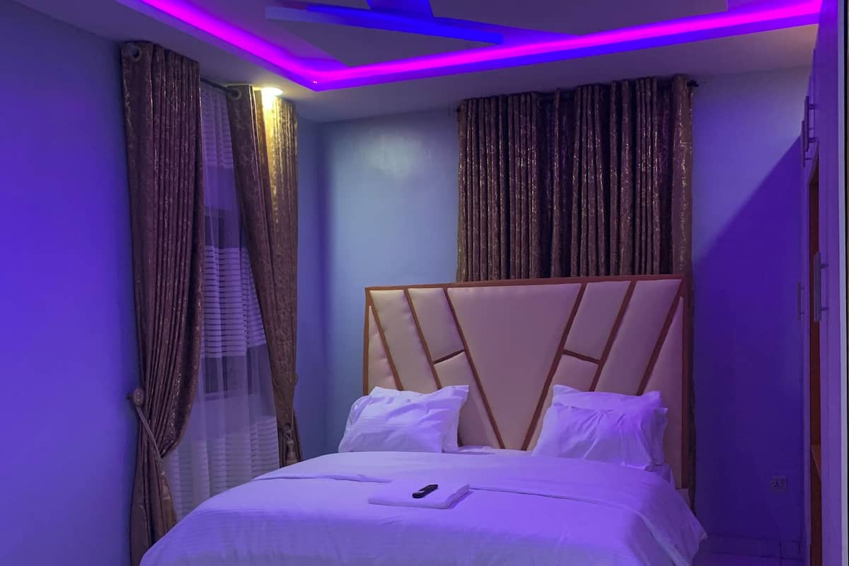 Quarto moderno com cama, cortinas e iluminação LED.