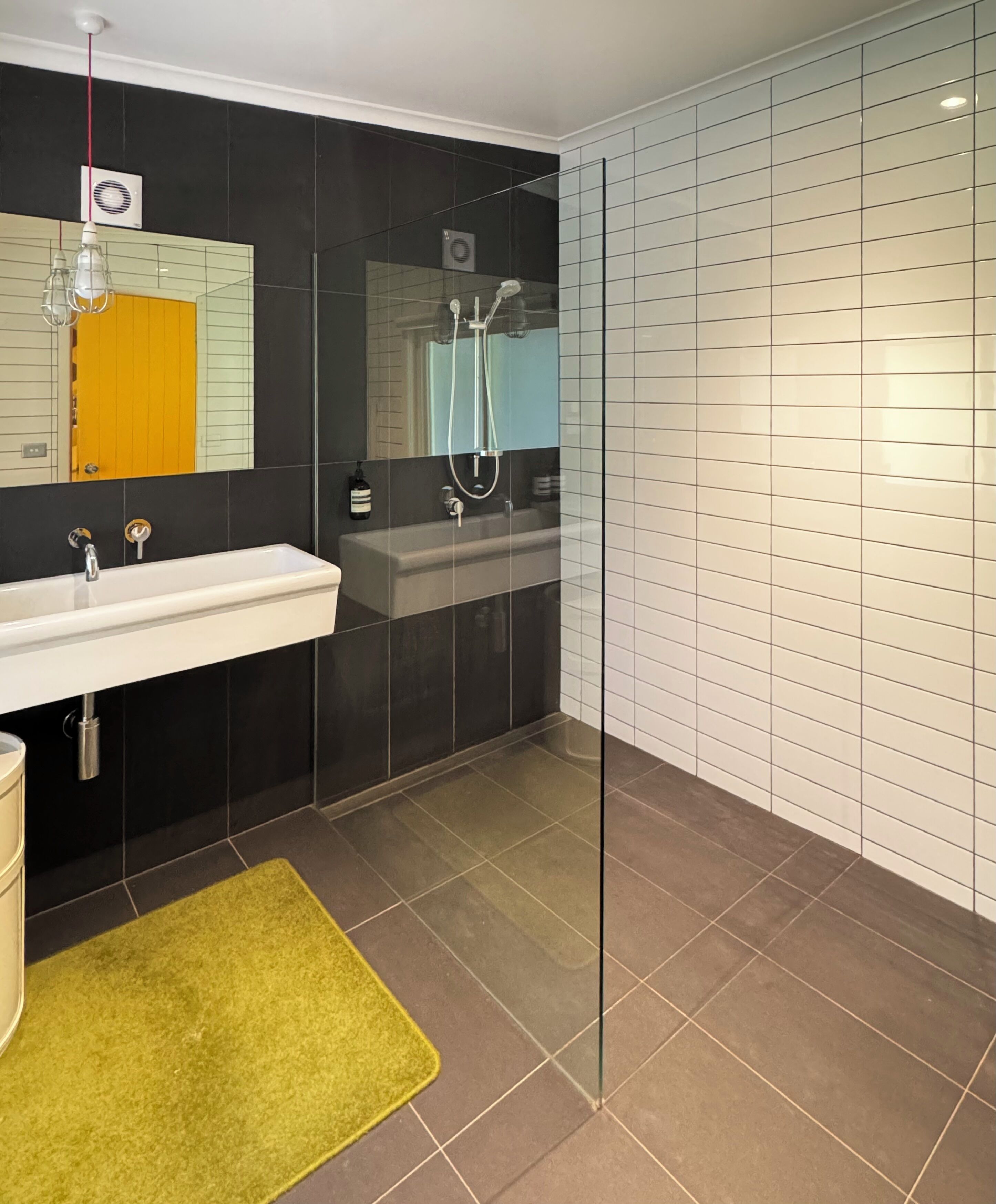 Un baño moderno con cabina de ducha de vidrio, un lavamanos blanco y una alfombra amarilla.