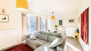 Un salon moderne avec un canapé d’angle gris, une moquette rouge et une suspension jaune.