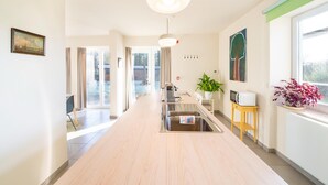 Une chambre d’hôtel moderne avec un plancher en bois, un coin cuisine équipé d’un évier et d’un four à micro-ondes, une table à manger et une grande fenêtre donnant sur l’extérieur.