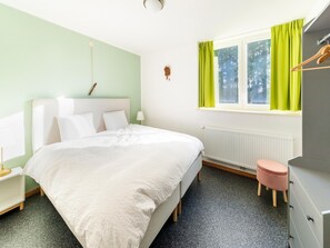 Ein Schlafzimmer mit Bett, Nachttisch, Kommode, Heizkörper und einem Fenster mit Vorhängen.
