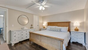 A bedroom with a large bed, two bedside tables, a ceiling fan, a mirror, and a dresser.