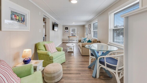 A spacious living area with a sofa, armchairs, a glass-top table, and a television mounted on the wall.
