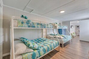 Habitación con literas, suelo de madera, paredes blancas y una puerta que da a otra habitación.