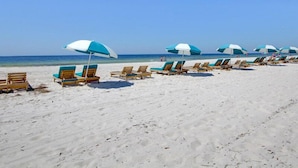 A beach with rows of wooden lounge chairs and blue and white umbrellas. - Turquoise Place #1107C | Gulf Front, Private Hot Tub + Resort Amenities (Orange Beach)