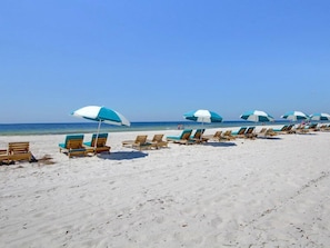 Une plage bordée de rangées de chaises longues en bois et d’ombrelles bleues et blanches.