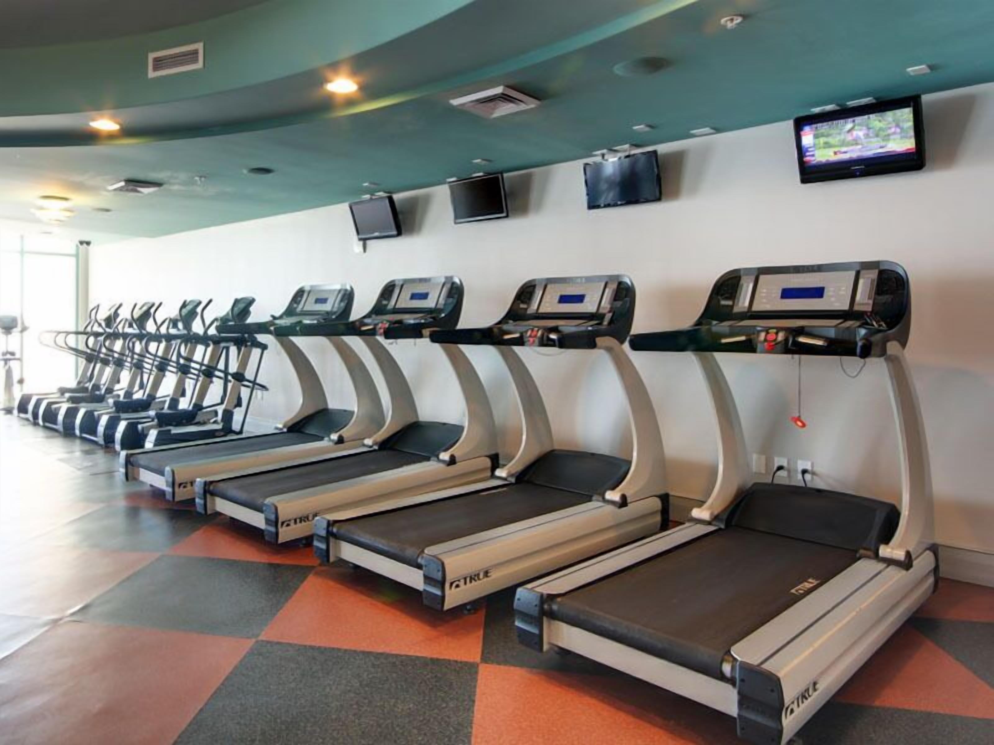 A row of treadmills in a gym with a checkered floor pattern.