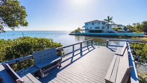 A wooden deck with benches overlooking a body of water and a white building with a blue roof. - 4-bedroom house on Longboat Key with private beach access only 150 yards away. (Longboat Key)