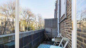 Un piccolo balcone con un tappeto decorato, una sedia in metallo e un tavolo.