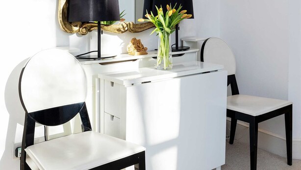 Un mobile bagno bianco con uno specchio dorato, lampade nere e un vaso con fiori gialli.