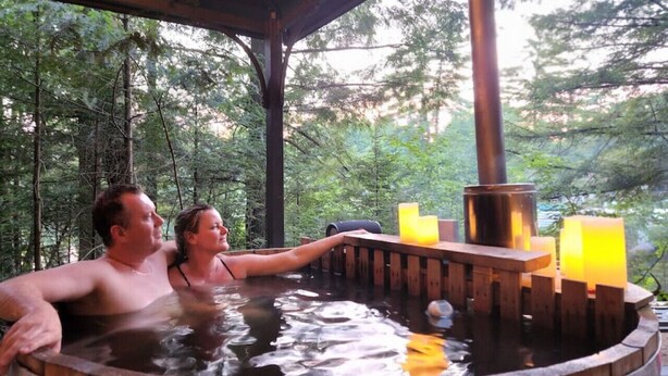 Un jacuzzi con estructura de madera y velas, rodeado de árboles.