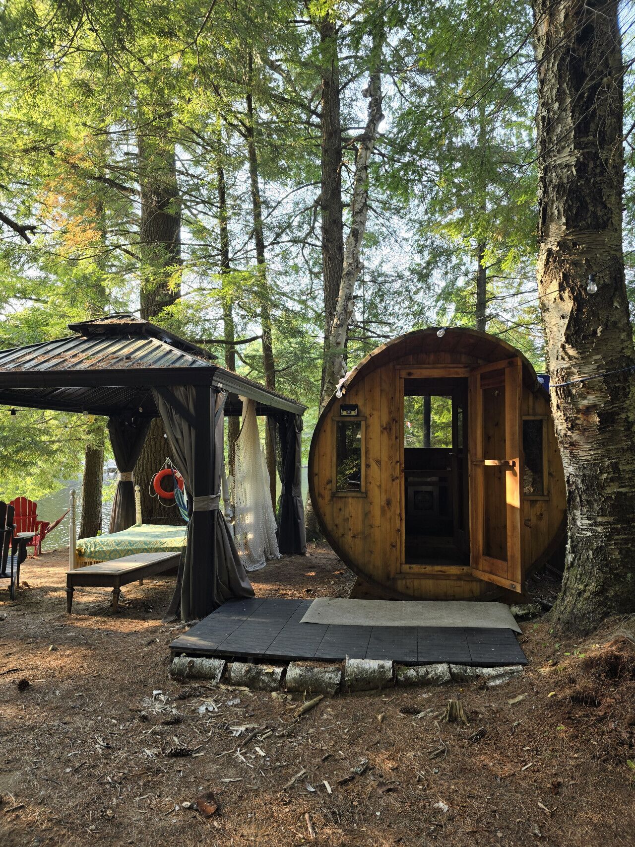 Una cabana rústica amb un petit porxo i un llit, envoltada d'arbres.