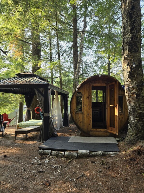 A rustic cabin with a small porch and a bed, surrounded by trees.