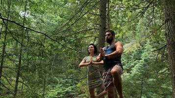 Two people standing on a rock in a forested area with a river in the background.