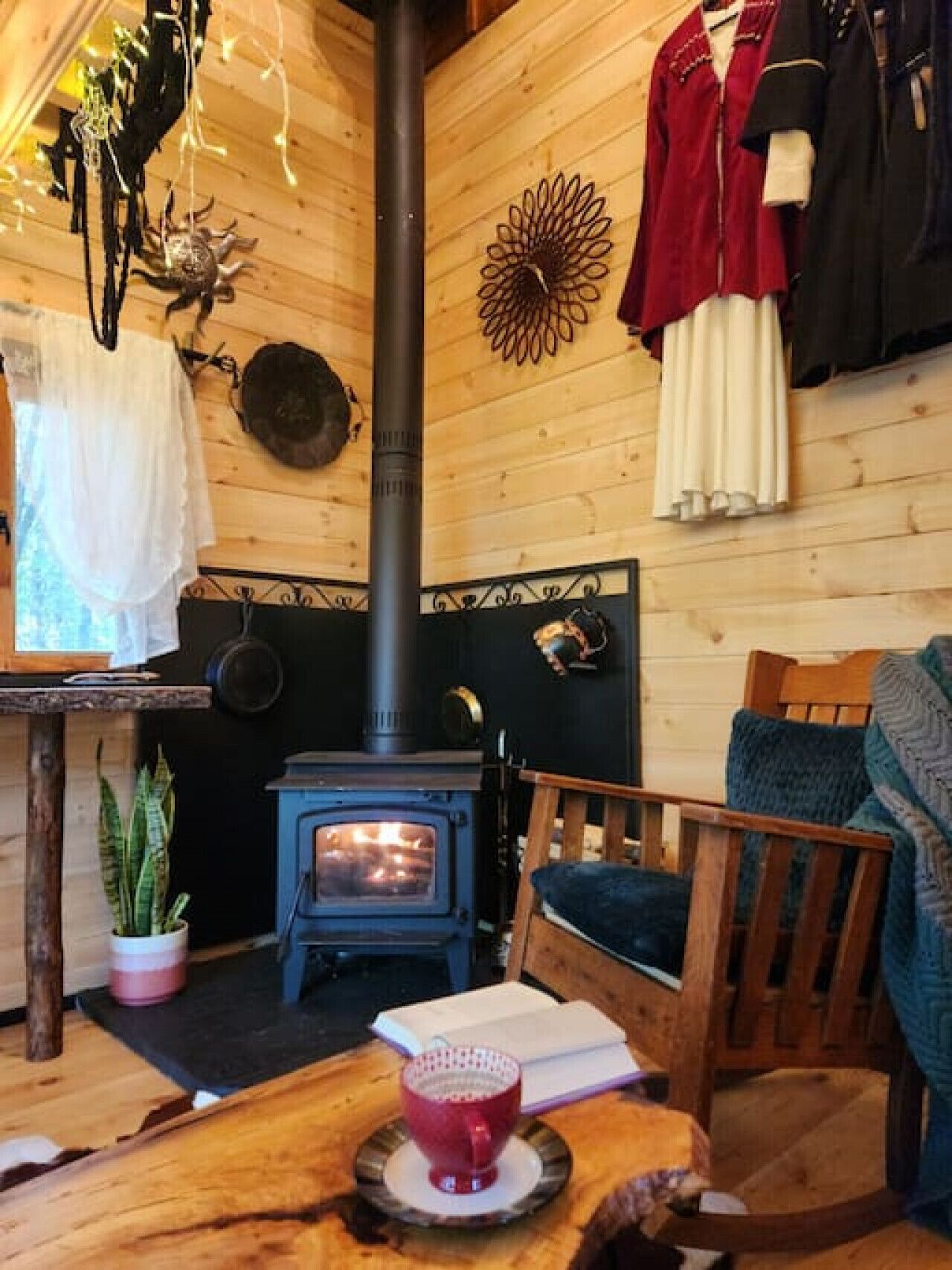 A cozy cabin interior with a wood-burning stove, wooden walls, a dining table with a cup, and a chair.