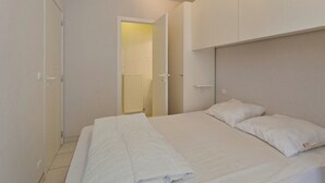 Un dormitorio con cama, ropa de cama blanca, cabecero y una puerta que da a un baño.