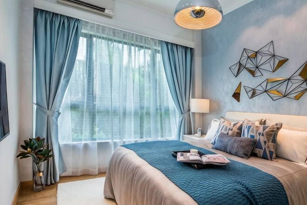Une chambre à coucher avec un lit, des rideaux, un tableau décoratif au mur, une table de chevet avec une lampe et une fenêtre donnant sur un paysage.