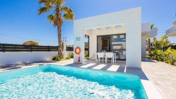Un área moderna junto a la piscina con una piscina azul cristalina, un flotador salvavidas y una mesa de comedor con sillas.