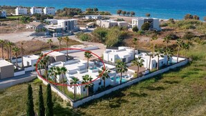 Una zona residencial costera con edificios blancos modernos, una piscina y palmeras.