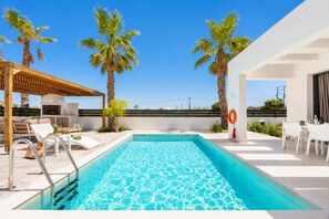 A swimming pool with a wooden pergola and lounge chairs, surrounded by palm trees and a clear sky. - Villa Salty Sun 2 - Two Bedroom Villa, Sleeps 4 (Kremasti)