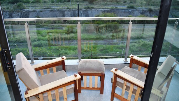 A balcony with two wooden chairs and a glass railing overlooking a landscape with greenery and a distant power line structure. - Sky park view apartment (Syokimau)