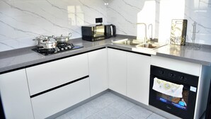 A modern kitchen with white cabinets, a gas stove, a microwave, a toaster, and a dishwasher. - Sky park view apartment (Syokimau)