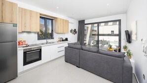Eine moderne Küche mit weißen Schränken, einem grauen Sofa und einem großen Fenster mit Blick auf einen Balkon.
