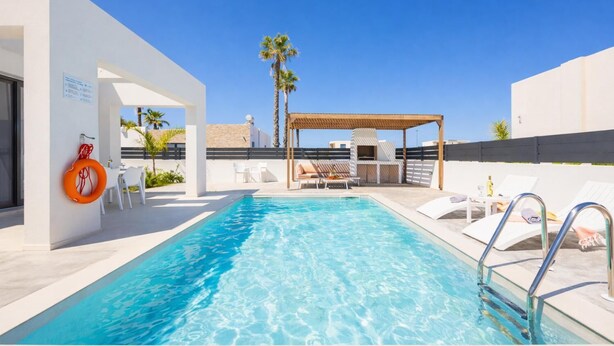 Ein Dachpool mit klarem, blauem Wasser, weißen Liegestühlen, einer Holzpergola und Palmen.