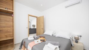 Ein modernes Hotelzimmer mit einem großen Bett, einem Holzschrank, einem Nachttisch mit Lampe und Blick ins Wohnzimmer.