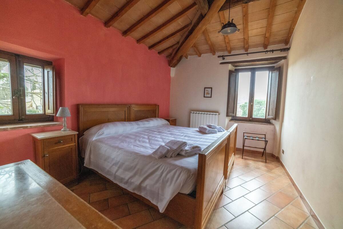 Ein Schlafzimmer mit einem hölzernen Bett, einem Nachttisch, einem Beistelltisch, einem Fenster und einer Heizung.