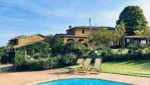 Una piscina con lettini, un edificio in pietra e un giardino curato.
