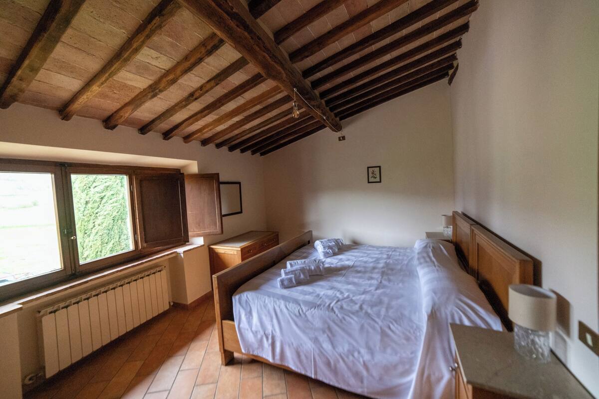 Ein Schlafzimmer mit Holzboden, einem großen Fenster, einem hölzernen Bett, einem Nachttisch und einer Heizung.