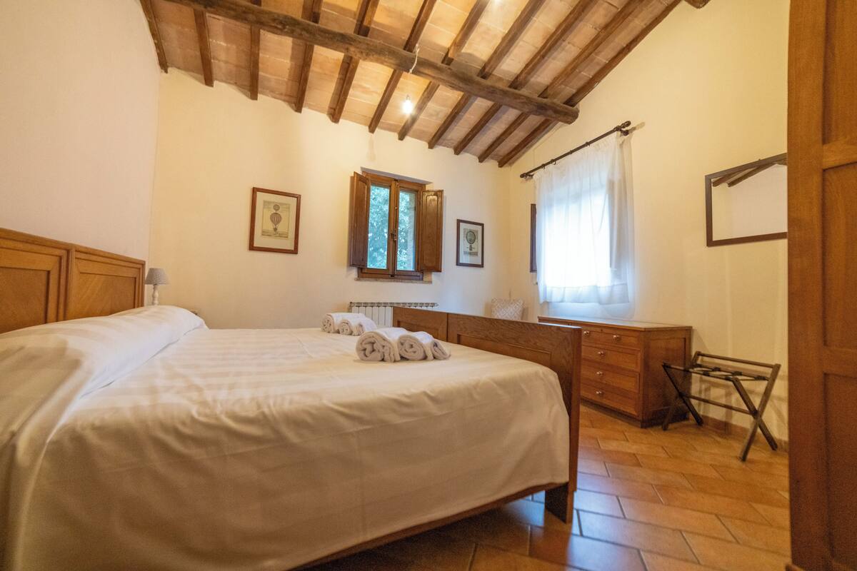 Ein Schlafzimmer mit einem hölzernen Bett, einem Schminktisch, einem Spiegel und einem Fenster mit Vorhängen.