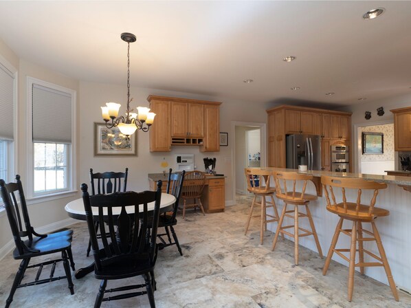 A kitchen with wooden cabinets, a central island with stools, a chandelier, and a dining table with chairs. - Guest Lodge | Private Pool | Outdoor Dining | Game Room (Sudlerville)
