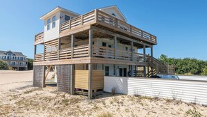 A two-story beach house with a wooden deck and a balcony. - Blue Moon - 4x4 Carova Beach, Ocean View, Pool, Hot Tub, Rec Room, Pool Table (4x4 - Carova NC)