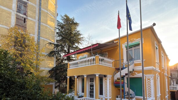 A yellow building with a balcony, a flagpole, and a staircase.