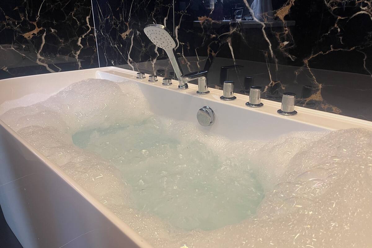 Une baignoire remplie de mousse, une douchette et plusieurs boutons de commande.