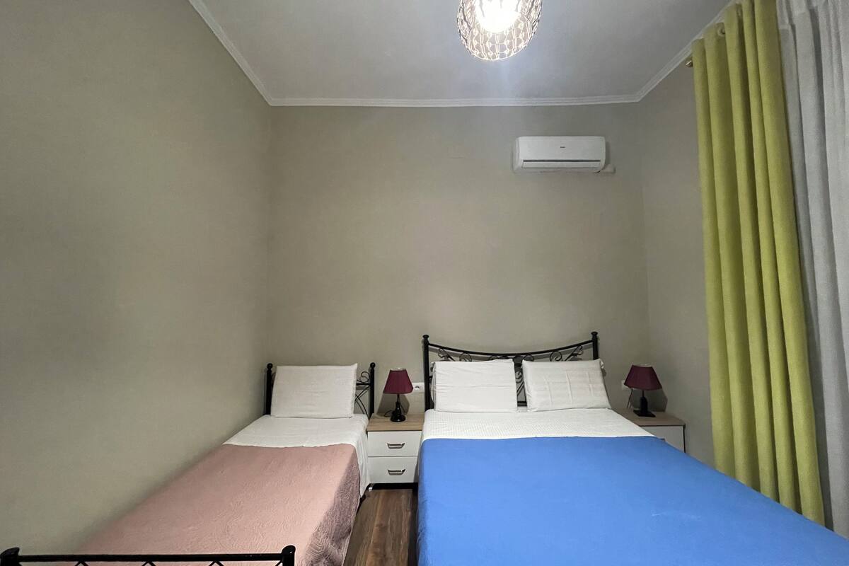 Une chambre avec deux lits, un luminaire au plafond, un appareil de climatisation et une table de chevet avec une lampe.