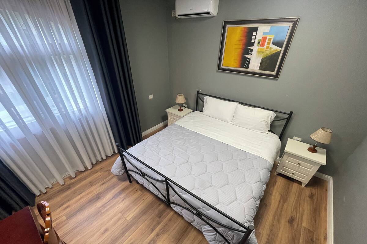 Une chambre à coucher bien rangée, avec un lit, des tables de chevet, une lampe et un tableau au mur.