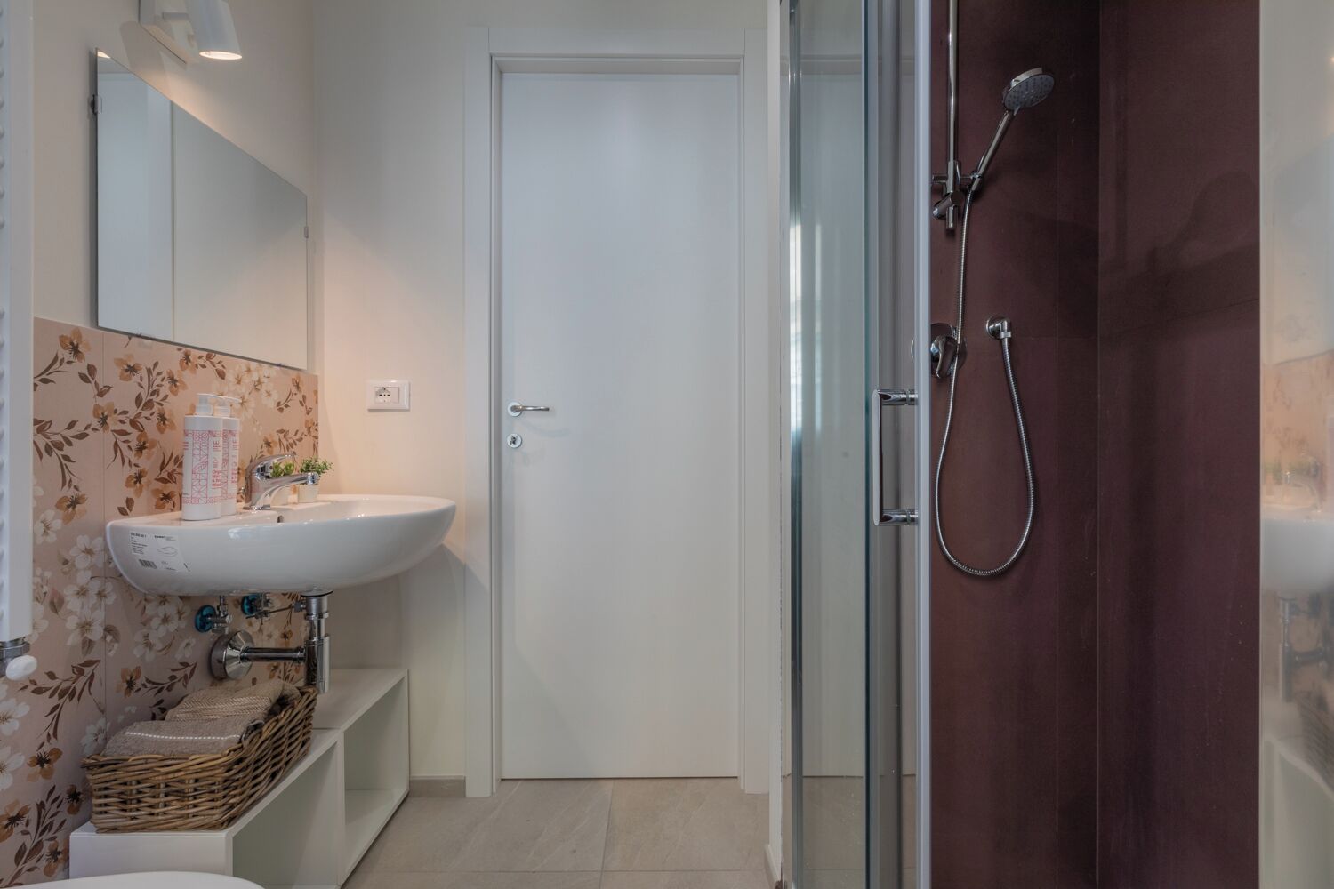 Une salle de bain avec un lavabo blanc, une cabine de douche en verre et une porte en bois.