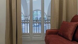 A room with a red sofa, a large window with a view of a balcony, and curtains. - Ai Portici di Susa by Wonderful Italy (Turin)